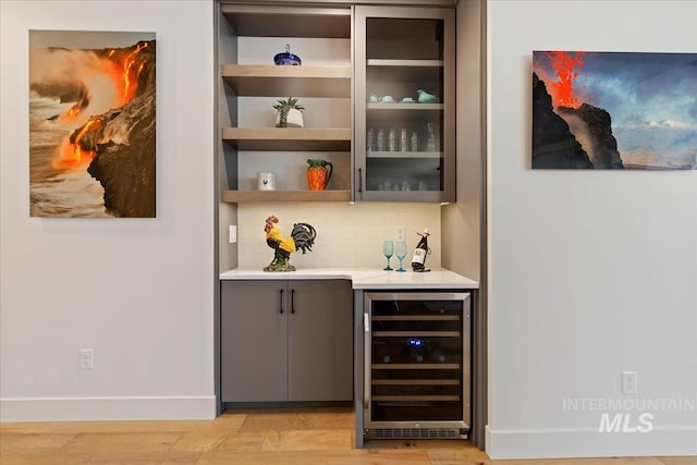 bar with a dry bar, baseboards, wine cooler, light wood-type flooring, and backsplash