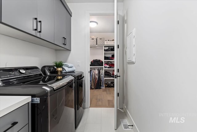 washroom with cabinet space, electric panel, baseboards, visible vents, and washer and clothes dryer