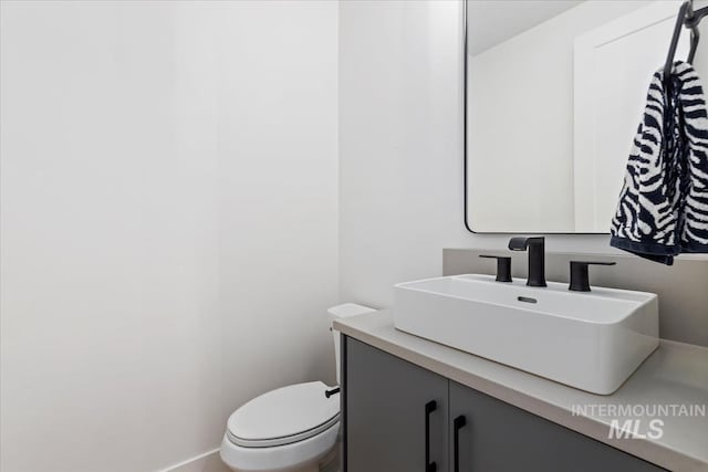 half bath featuring baseboards, vanity, and toilet