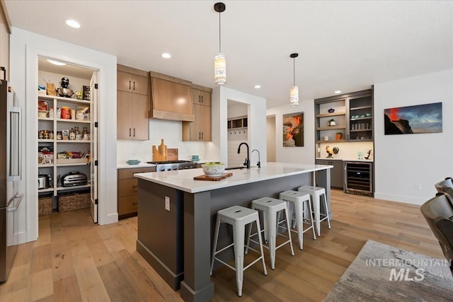 kitchen with light wood-style flooring, beverage cooler, custom exhaust hood, open shelves, and a kitchen bar