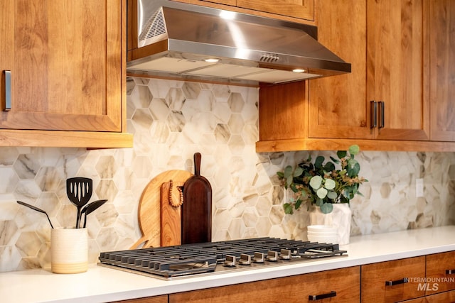 kitchen featuring under cabinet range hood, decorative backsplash, brown cabinets, and light countertops