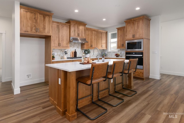 kitchen featuring under cabinet range hood, tasteful backsplash, dark wood finished floors, stainless steel appliances, and light countertops