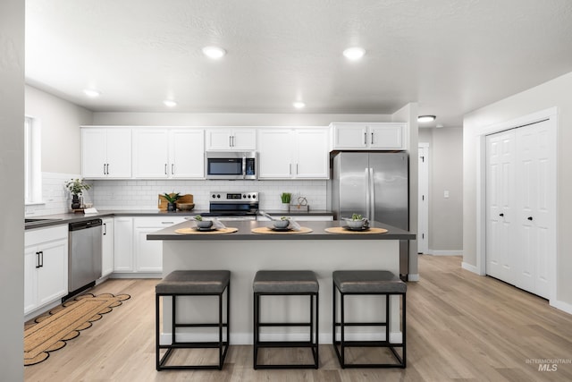 19920 Lenape Ct, Caldwell, ID 83605 - kitchen featuring appliances with stainless steel finishes, dark countertops, a kitchen bar, white cabinetry, and tasteful backsplash