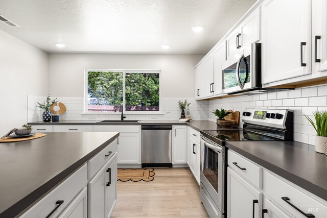 19920 Lenape Ct, Caldwell, ID 83605 - kitchen with stainless steel appliances, a sink, dark countertops, light wood finished floors, and white cabinets