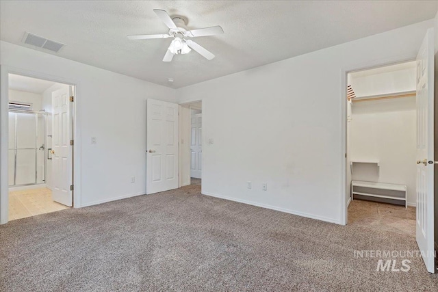 unfurnished bedroom featuring a spacious closet, light carpet, a textured ceiling, and ensuite bath