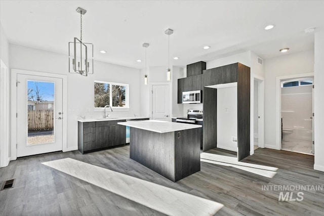 kitchen with decorative light fixtures, sink, dark wood-type flooring, a center island, and stainless steel appliances