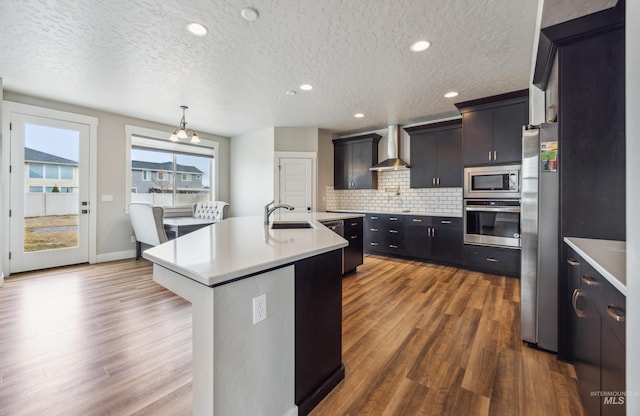 kitchen featuring a sink, stainless steel appliances, wall chimney exhaust hood, light countertops, and decorative backsplash