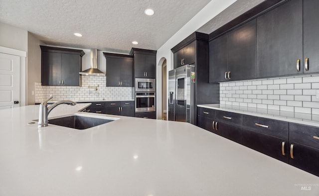 kitchen featuring light countertops, wall chimney range hood, appliances with stainless steel finishes, and a sink