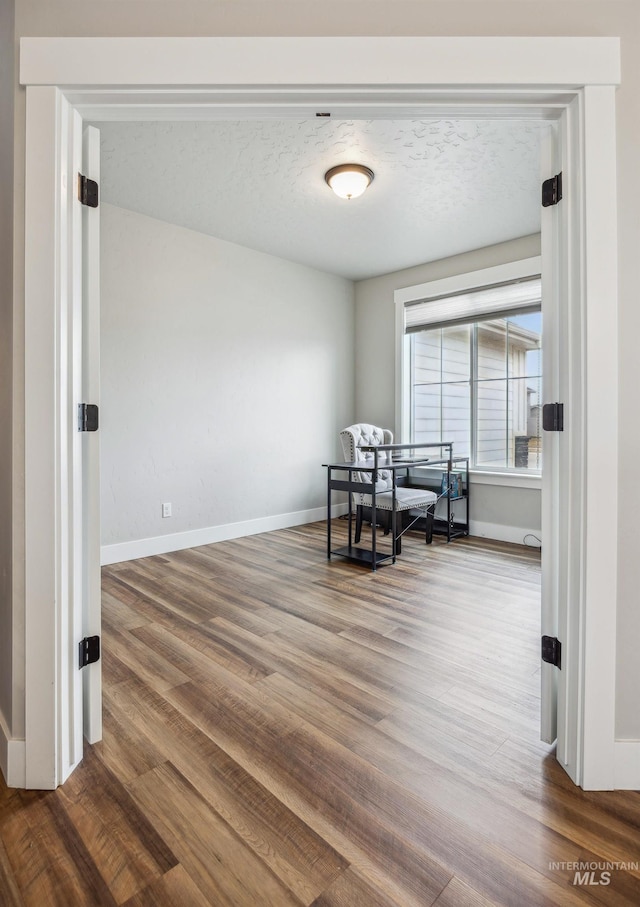 unfurnished room with a textured ceiling, baseboards, and wood finished floors