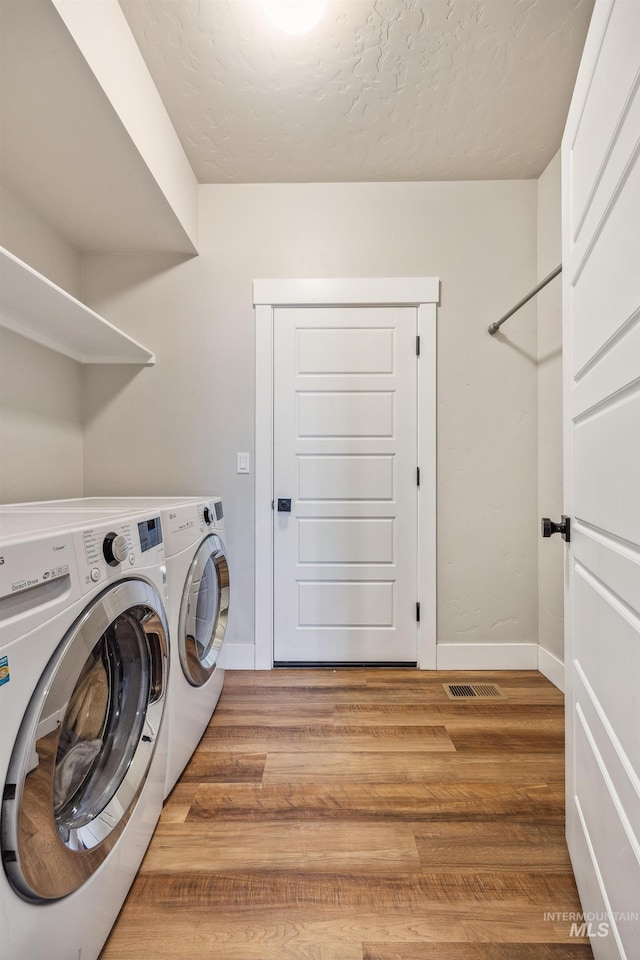 laundry room with light wood-type flooring, visible vents, baseboards, laundry area, and washing machine and clothes dryer