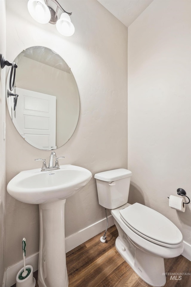 half bathroom featuring a sink, toilet, baseboards, and wood finished floors