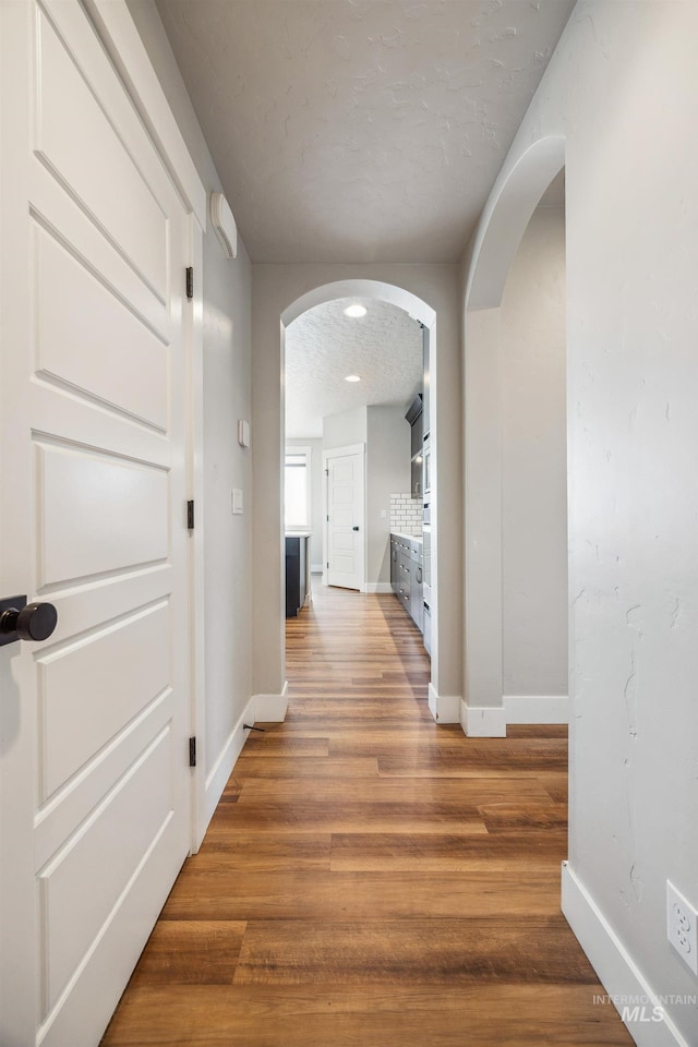 hall with arched walkways, a textured ceiling, light wood-type flooring, and baseboards