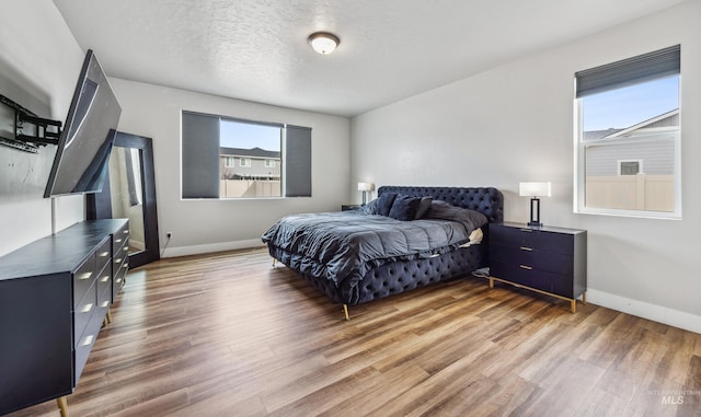 bedroom with light wood-style floors, baseboards, and a textured ceiling