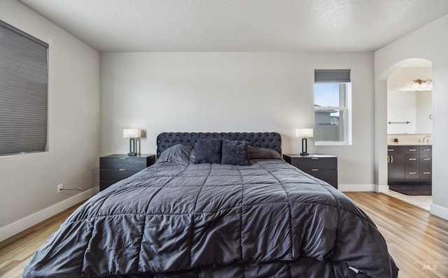 bedroom with light wood-style floors, arched walkways, and baseboards