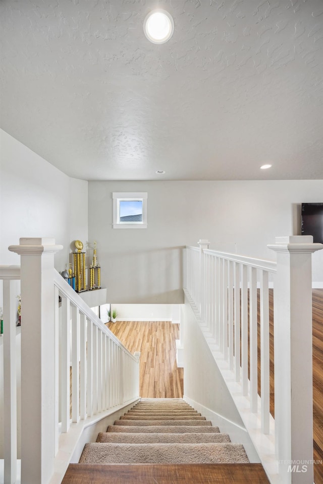 staircase featuring recessed lighting, wood finished floors, baseboards, and a textured ceiling