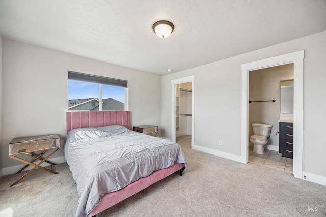 bedroom with a spacious closet, light colored carpet, baseboards, and ensuite bathroom