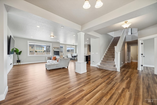 unfurnished living room with stairway, baseboards, ornate columns, and wood finished floors