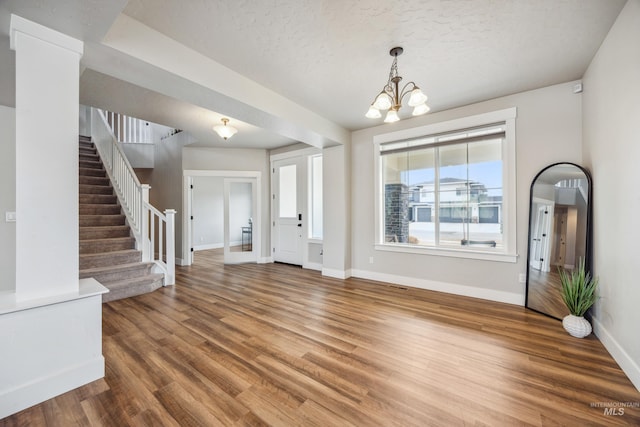 entrance foyer featuring baseboards, a chandelier, stairway, wood finished floors, and a textured ceiling