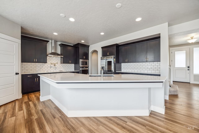 kitchen featuring a sink, arched walkways, appliances with stainless steel finishes, wall chimney exhaust hood, and light countertops