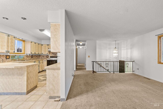 kitchen with light brown cabinetry, light colored carpet, and a textured ceiling