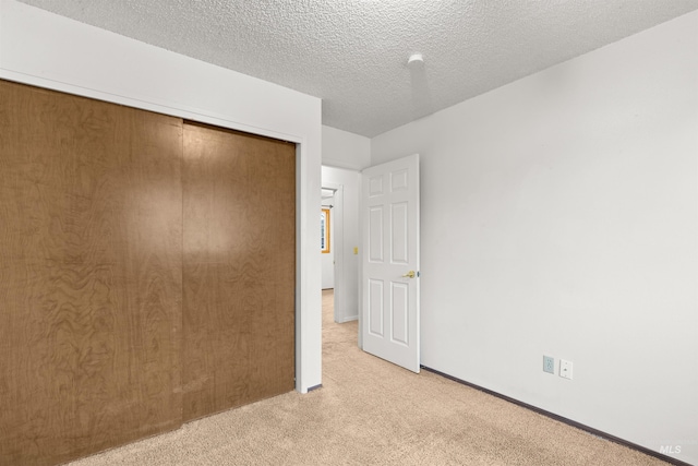 unfurnished bedroom featuring a textured ceiling, light colored carpet, and a closet