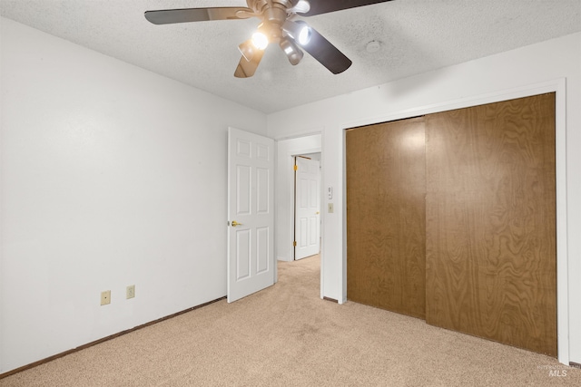 unfurnished bedroom featuring ceiling fan, a closet, light colored carpet, and a textured ceiling