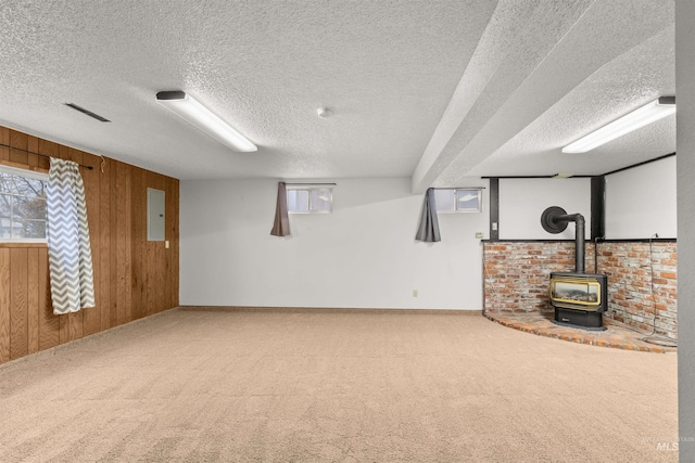 basement with wood walls, a wood stove, electric panel, carpet flooring, and a textured ceiling