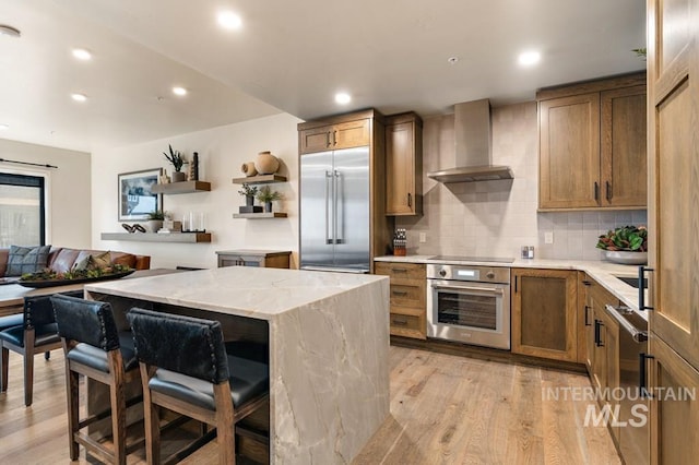 kitchen featuring a breakfast bar, light wood-type flooring, appliances with stainless steel finishes, a kitchen island, and wall chimney range hood