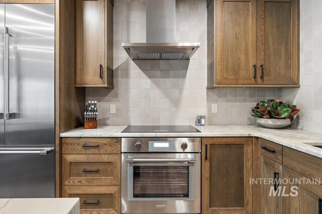 kitchen with tasteful backsplash, wall chimney range hood, light stone counters, and stainless steel appliances