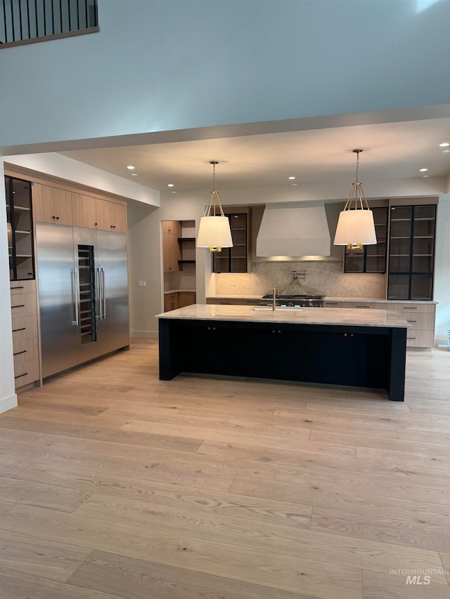 kitchen featuring stainless steel built in fridge, decorative light fixtures, wall chimney exhaust hood, and light hardwood / wood-style flooring