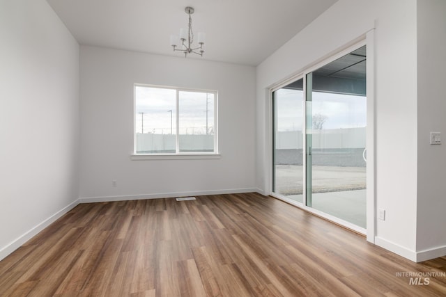 empty room featuring an inviting chandelier, a wealth of natural light, and wood finished floors