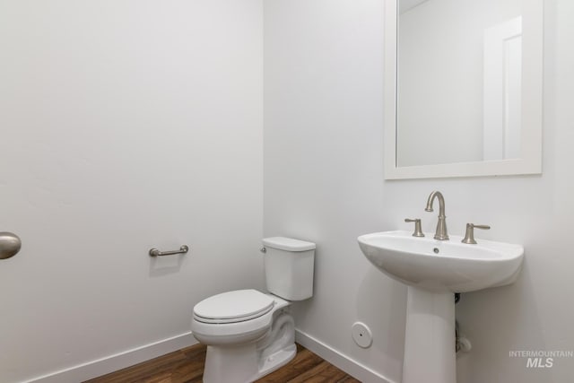 half bath with toilet, baseboards, and wood finished floors