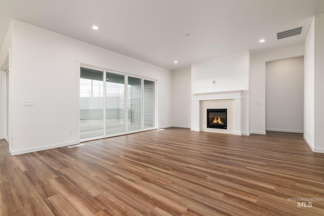 unfurnished living room with a glass covered fireplace, recessed lighting, wood finished floors, and visible vents