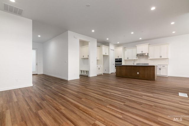 unfurnished living room with visible vents, a sink, baseboards, dark wood-style floors, and recessed lighting