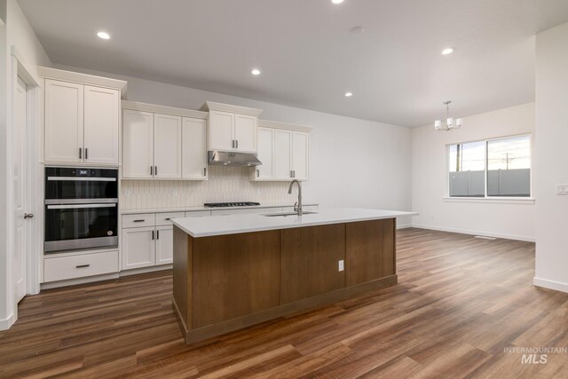 kitchen with backsplash, dark wood finished floors, gas stovetop, a sink, and under cabinet range hood