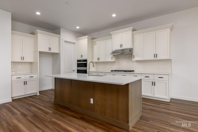 kitchen featuring a sink, white cabinetry, backsplash, under cabinet range hood, and dark wood-style floors
