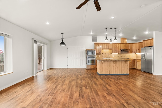 kitchen with vaulted ceiling, a kitchen island, appliances with stainless steel finishes, pendant lighting, and decorative backsplash