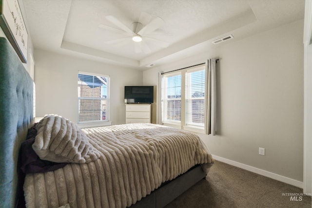 bedroom with a raised ceiling, dark carpet, ceiling fan, and multiple windows