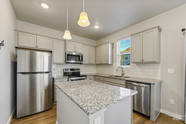 kitchen with sink, light stone counters, a center island, hanging light fixtures, and appliances with stainless steel finishes