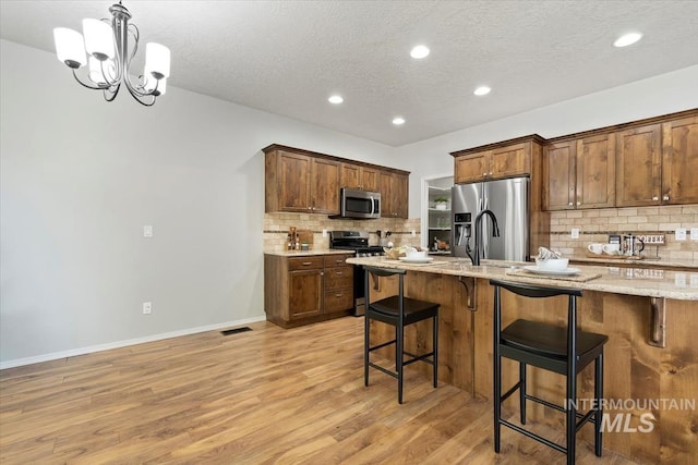 kitchen featuring stainless steel appliances, decorative backsplash, light wood-style flooring, a kitchen bar, and a textured ceiling