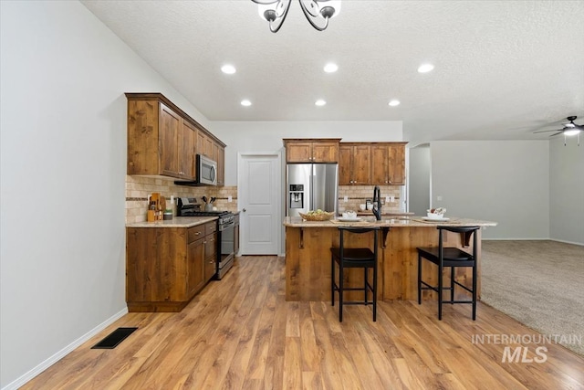 kitchen featuring stainless steel appliances, tasteful backsplash, a breakfast bar, light wood-style flooring, and a kitchen island with sink