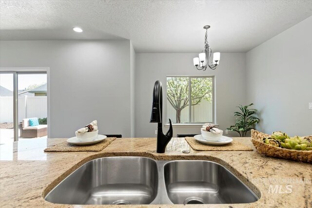 kitchen view of a sink, light stone countertops, hanging light fixtures, a chandelier, and recessed lighting