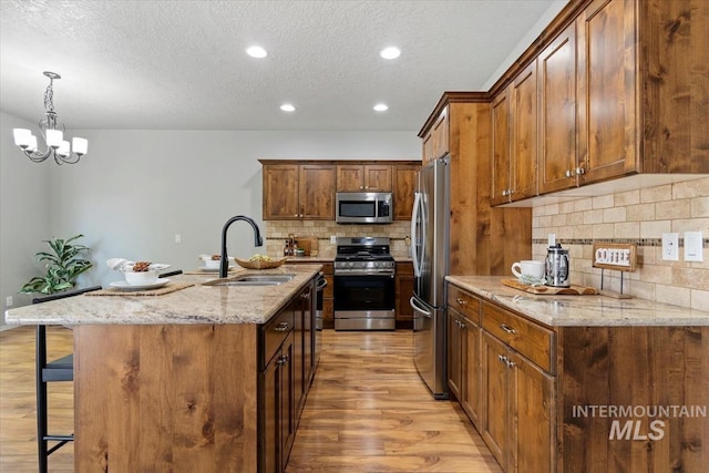 kitchen featuring stainless steel appliances, a sink, light wood-type flooring, a kitchen bar, and backsplash
