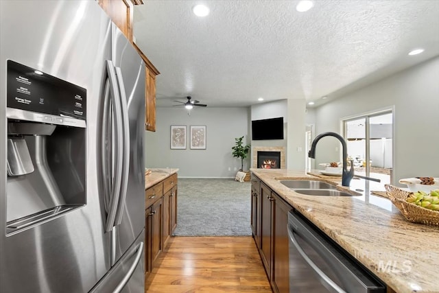 kitchen featuring stainless steel appliances, a sink, a textured ceiling, a glass covered fireplace, and light stone counters