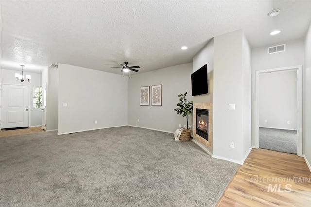 unfurnished living room with carpet, a textured ceiling, a tile fireplace, a chandelier, and a ceiling fan