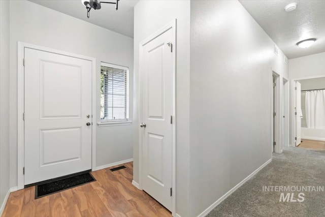 foyer featuring baseboards, light wood-type flooring, and a textured ceiling