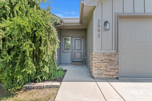 view of exterior entry with board and batten siding, a garage, and stone siding