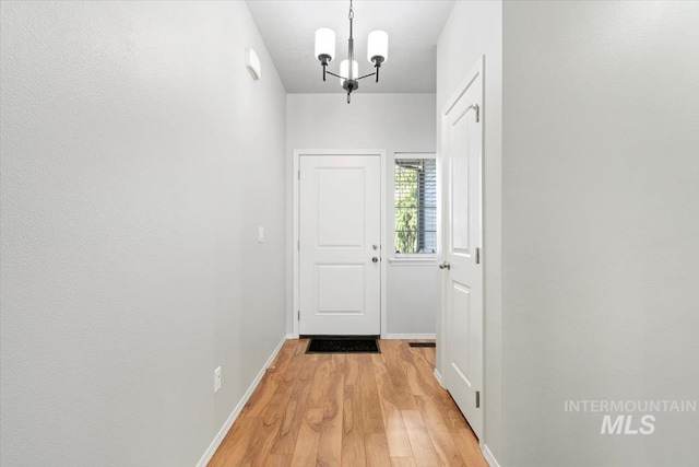 doorway with light wood-style flooring, baseboards, and a chandelier