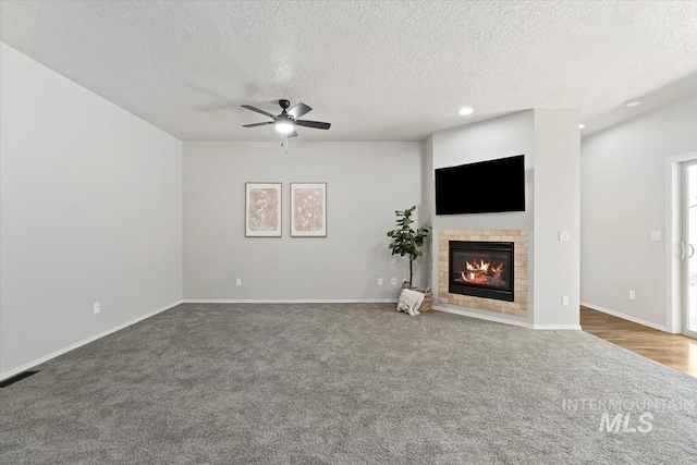 unfurnished living room featuring carpet floors, a glass covered fireplace, ceiling fan, a textured ceiling, and recessed lighting