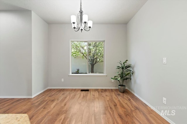 unfurnished room featuring a chandelier, wood finished floors, and baseboards